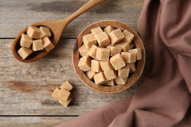 Photo of Bowl and spoon with brown sugar cubes on wooden table, flat lay