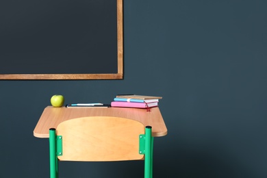 Photo of Wooden school desk with stationery and apple near blackboard on grey wall