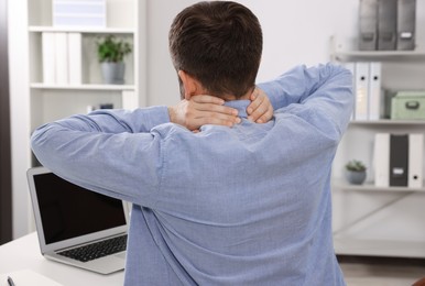 Man suffering from neck pain in office, back view