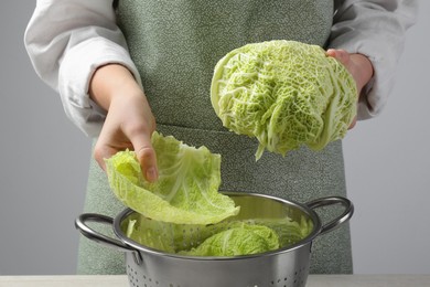 Photo of Woman putting leaf from fresh savoy cabbage at wooden table, closeup