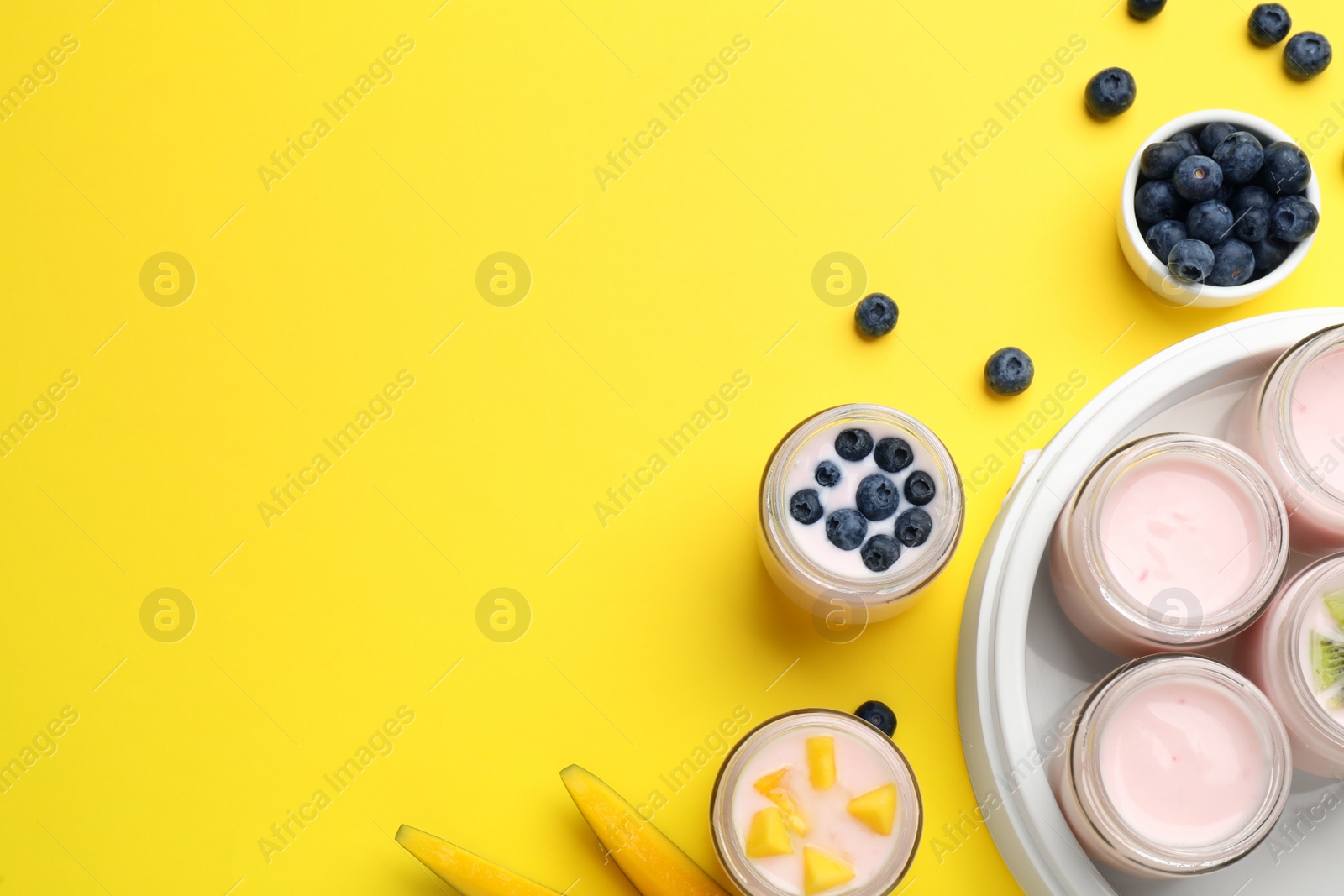 Photo of Tasty yogurt in glass jars and ingredients on yellow background, flat lay. Space for text