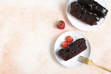 Pieces of chocolate sponge cake and strawberries on beige textured table, flat lay. Space for text