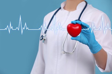 Image of Doctor holding red heart on light blue background, closeup