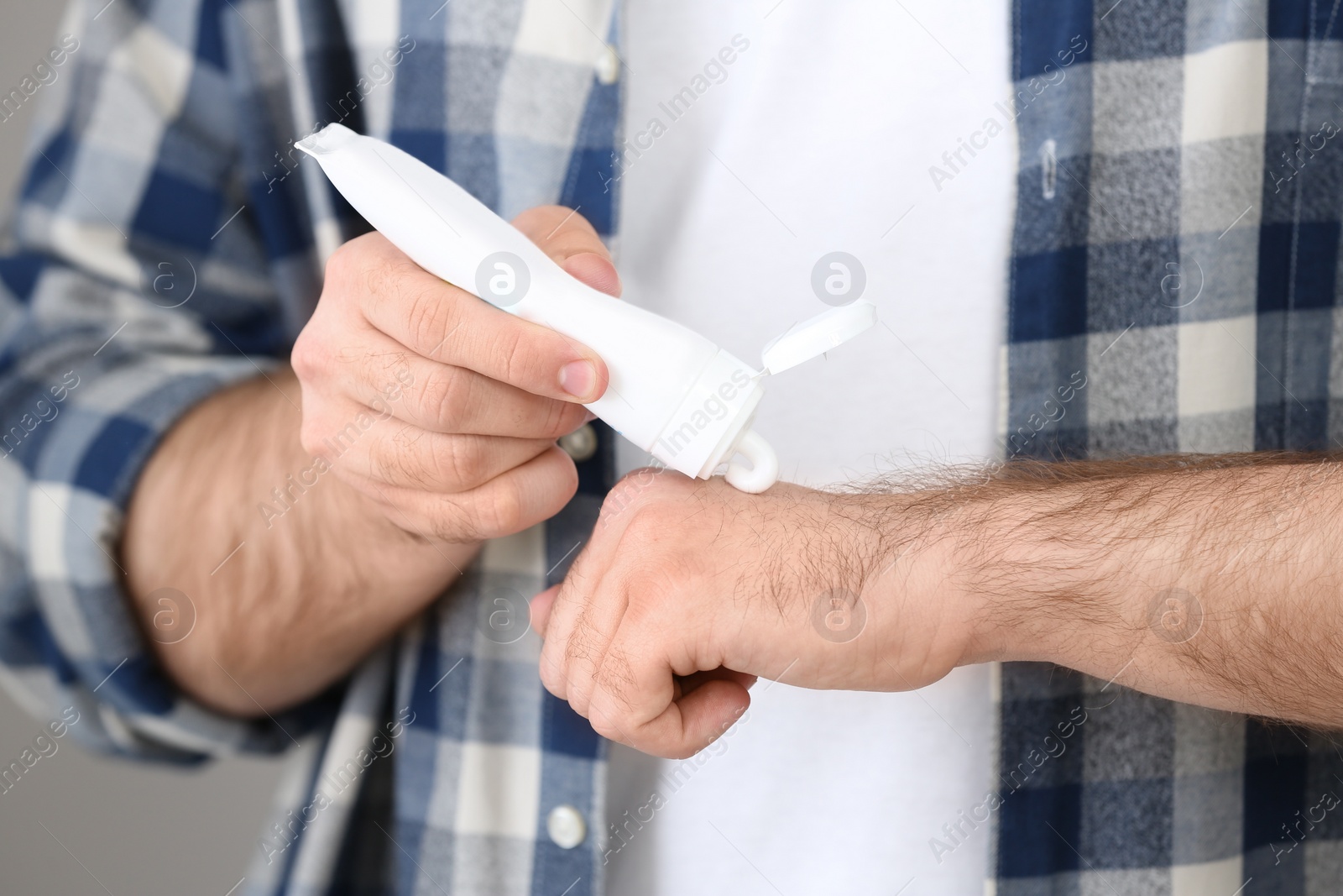 Photo of Man applying cream from tube onto hand on light grey background, closeup