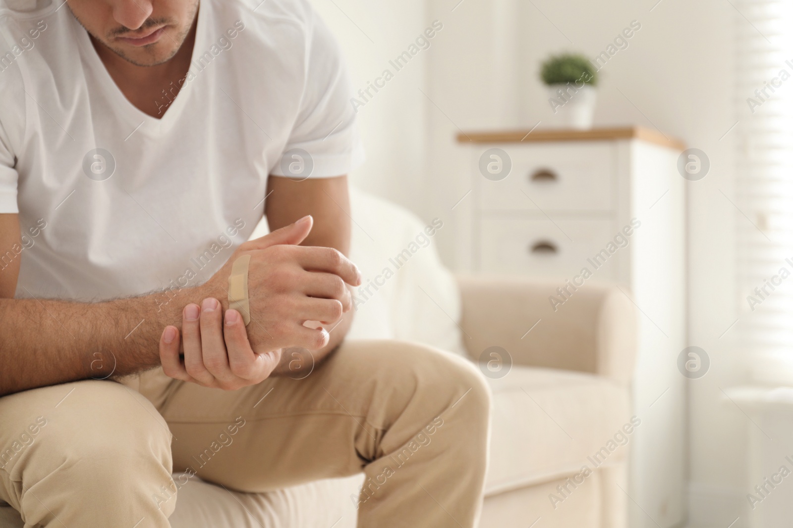 Photo of Man putting sticking plaster onto hand indoors, closeup