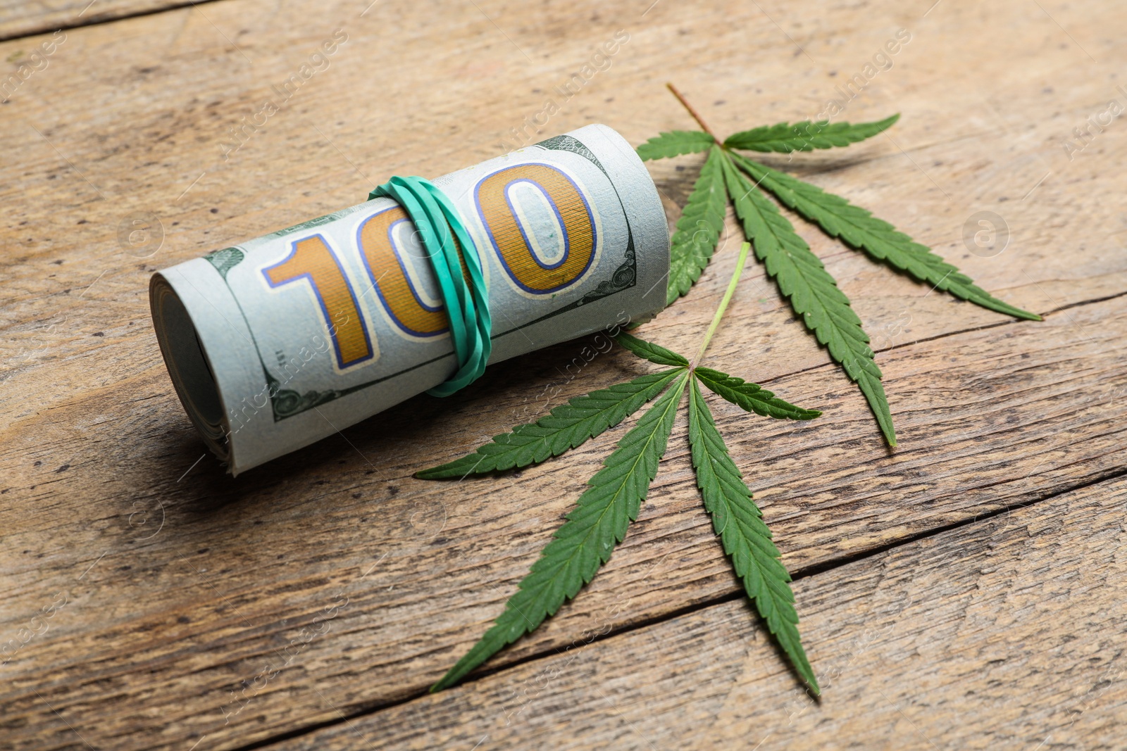 Photo of Hemp leaves and rolled money on wooden background, closeup