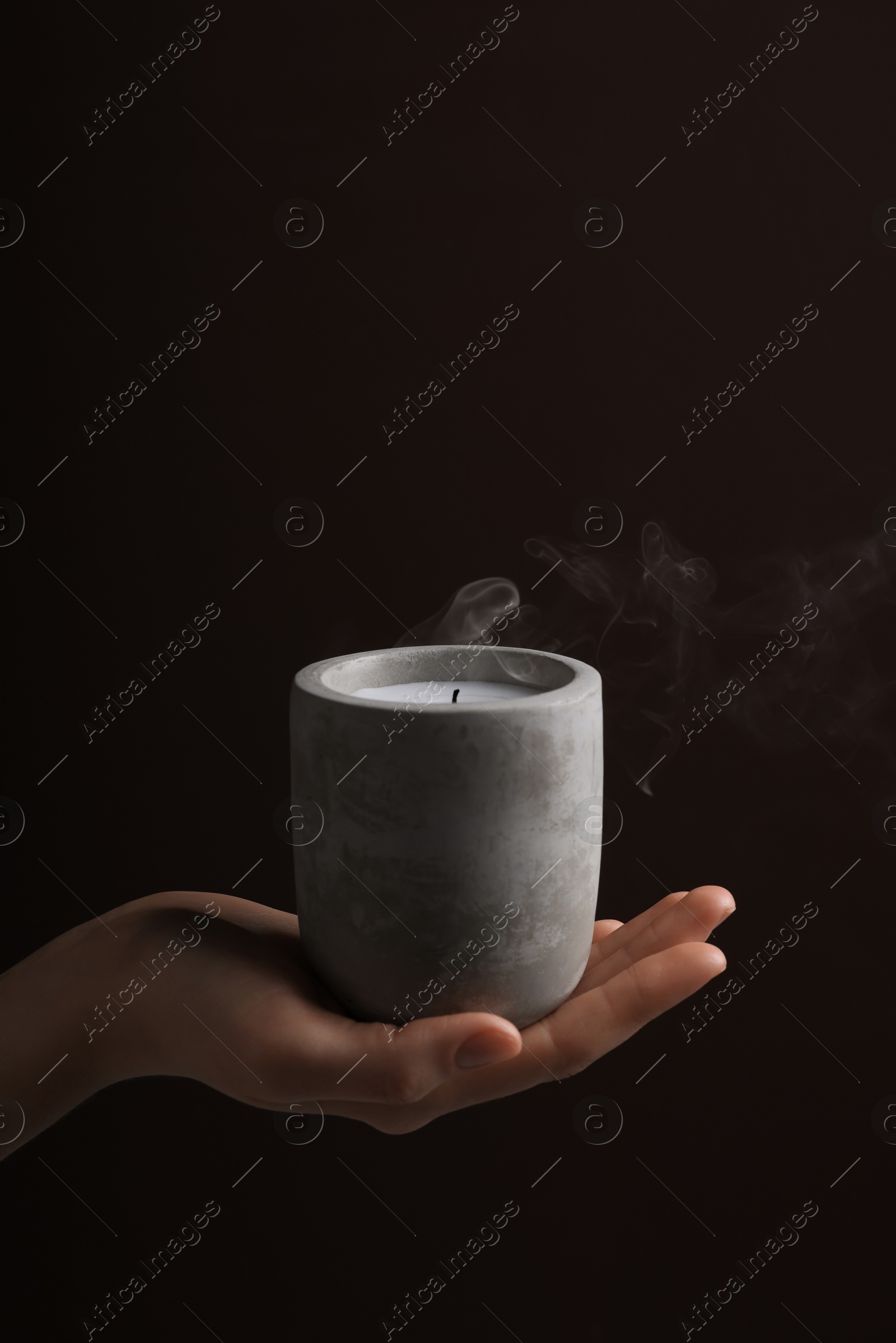 Photo of Woman with blown out candle in concrete holder against dark brown background, closeup