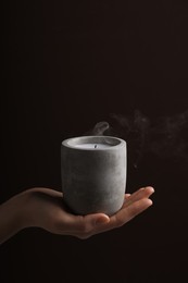 Woman with blown out candle in concrete holder against dark brown background, closeup