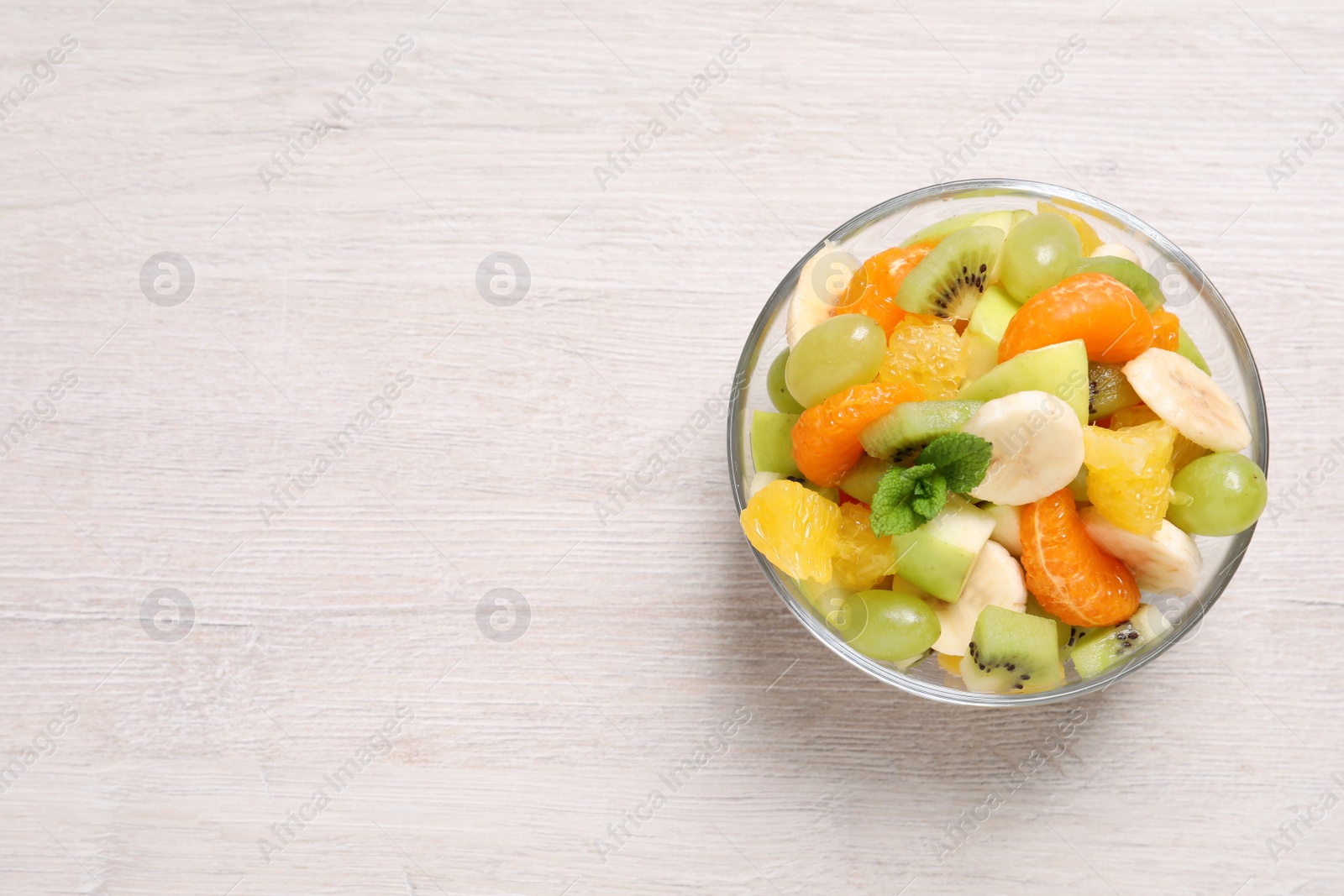 Photo of Delicious fresh fruit salad in bowl on white wooden table, top view. Space for text