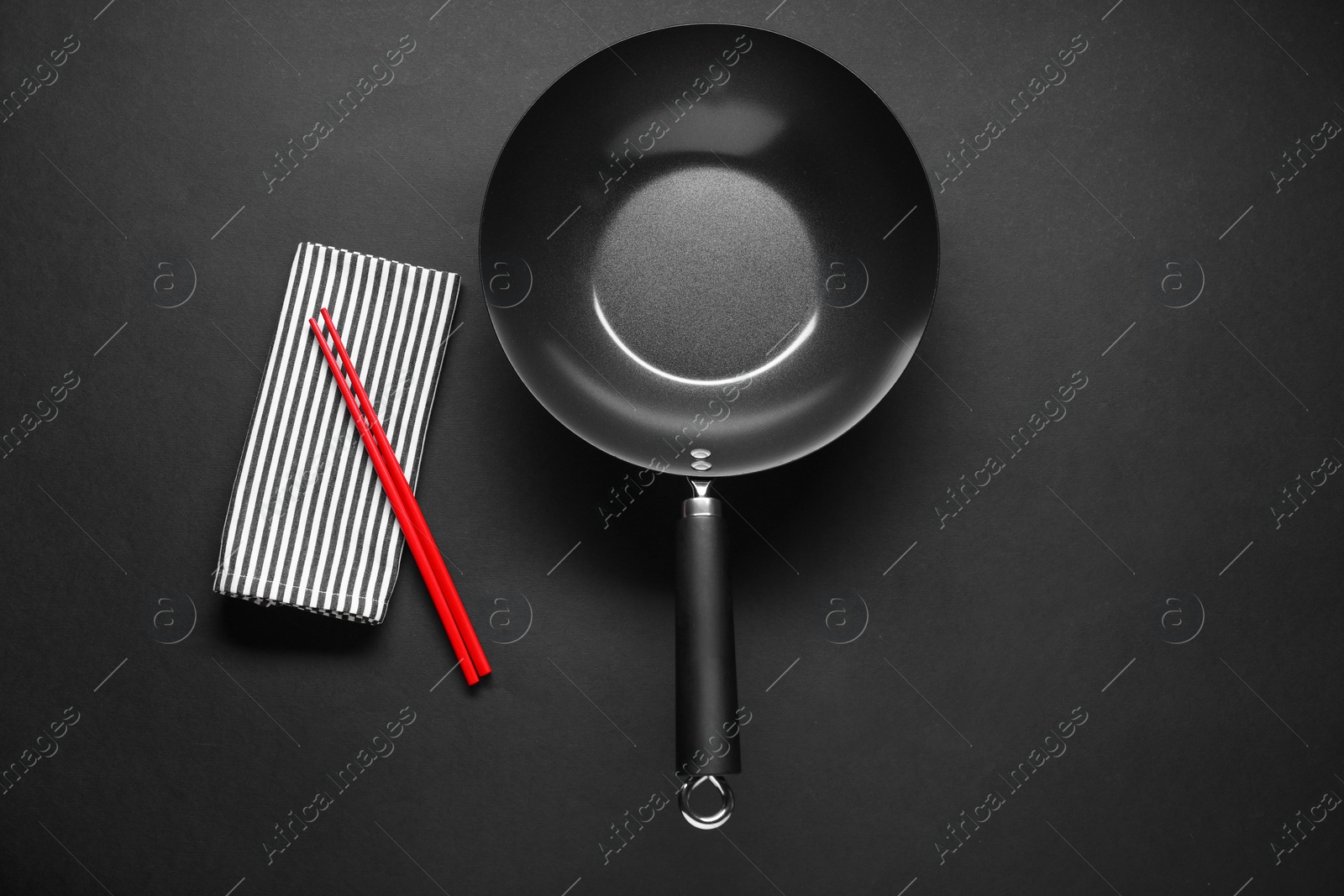 Photo of Empty iron wok and chopsticks on black table, flat lay