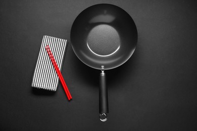 Photo of Empty iron wok and chopsticks on black table, flat lay