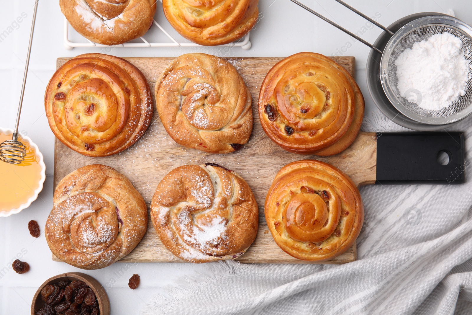 Photo of Delicious rolls with raisins and powdered sugar on white table, flat lay. Sweet buns