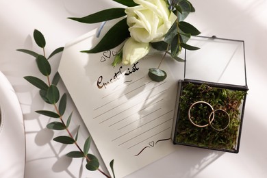 Image of Beautiful wedding rings, boutonniere and guest list on white background, top view
