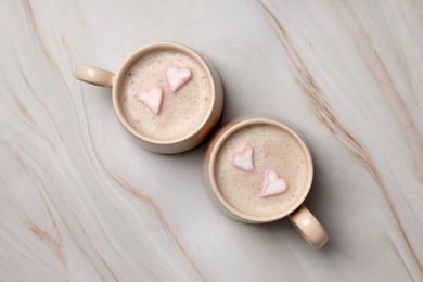 Photo of Cups of aromatic coffee with heart shaped marshmallows on white marble table, flat lay