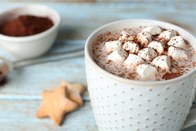 Delicious hot cocoa drink with marshmallows in cup on light blue wooden table, closeup