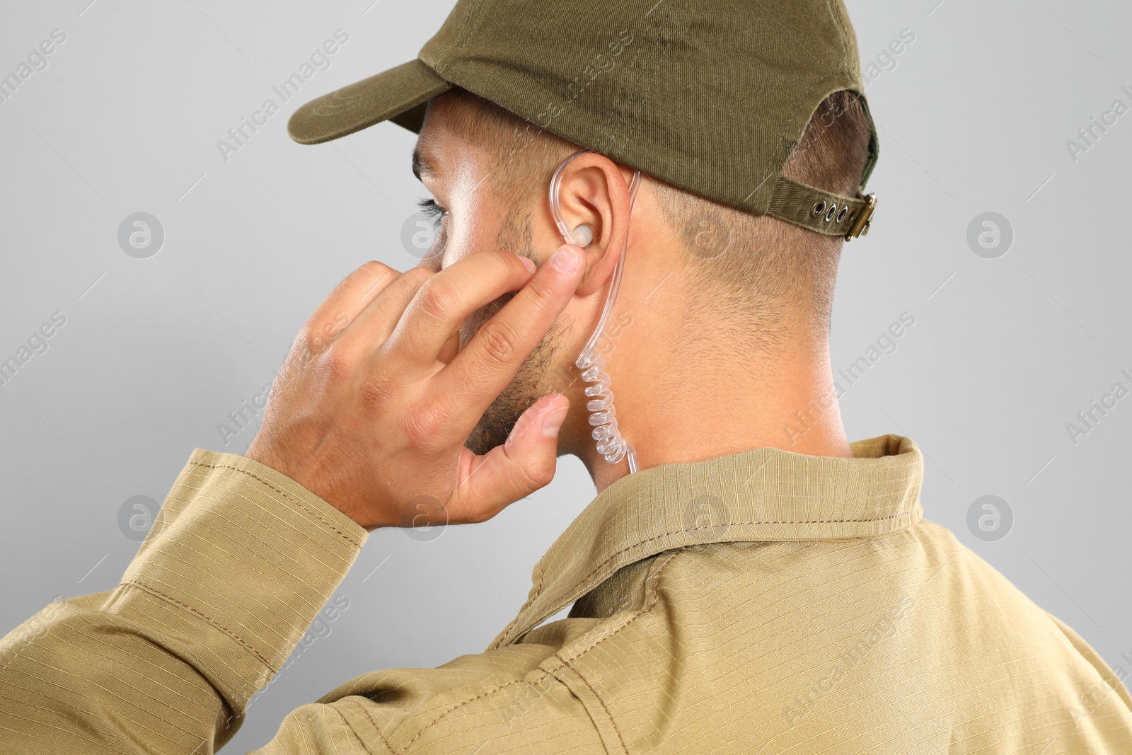 Photo of Male security guard in uniform using radio earpiece on grey background, closeup