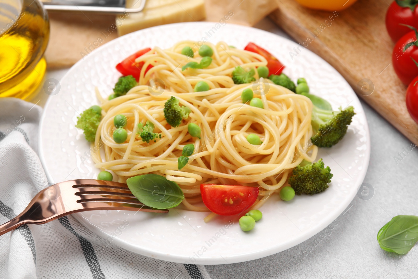 Photo of Plate of delicious pasta primavera and ingredients on light gray table, closeup