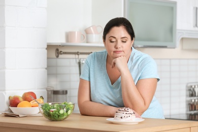 Photo of Woman choosing between vegetable salad and dessert in kitchen. Healthy diet