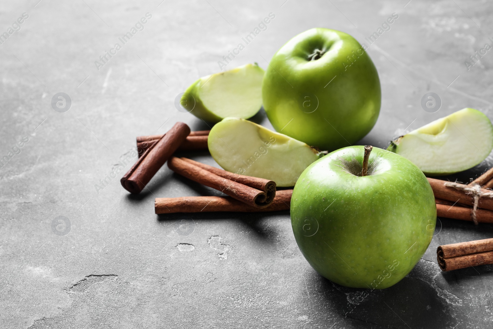 Photo of Fresh apples and cinnamon sticks on gray table