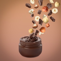 Making yummy chocolate paste. Hazelnuts and pieces of chocolate falling into jar on light brown background