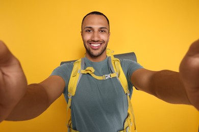 Happy tourist with backpack taking selfie on yellow background