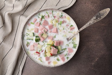 Photo of Delicious cold summer soup (okroshka) with boiled sausage and spoon in bowl on brown table, top view