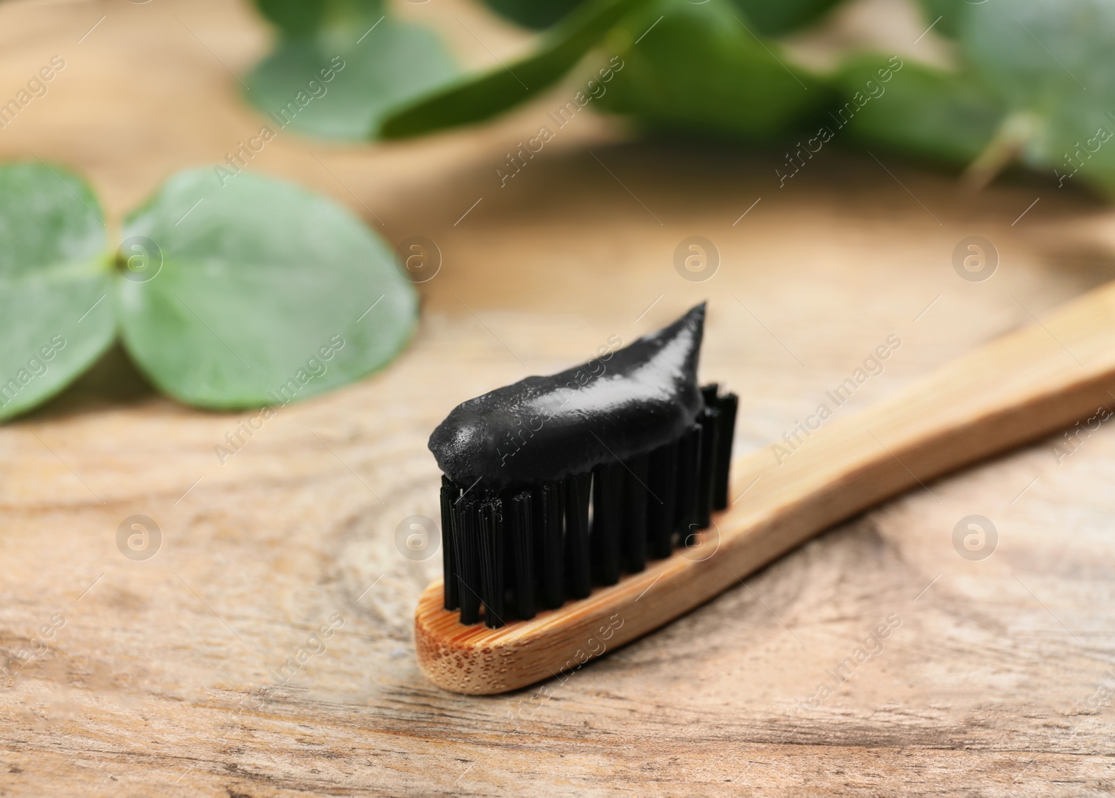 Photo of Bamboo toothbrush with charcoal paste on wooden  table, closeup. Space for text