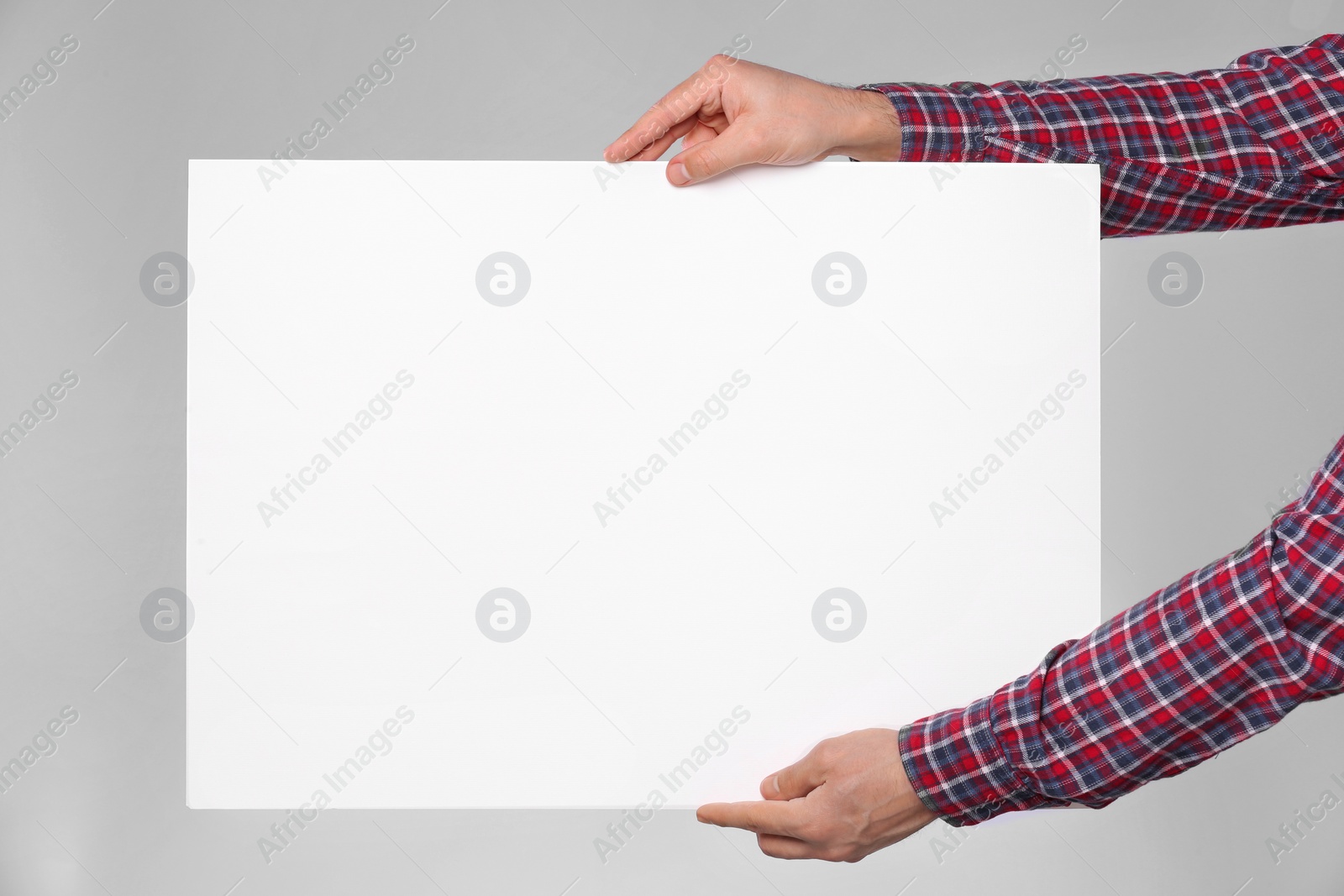 Photo of Man holding sheet of paper on grey background, closeup. Mockup for design