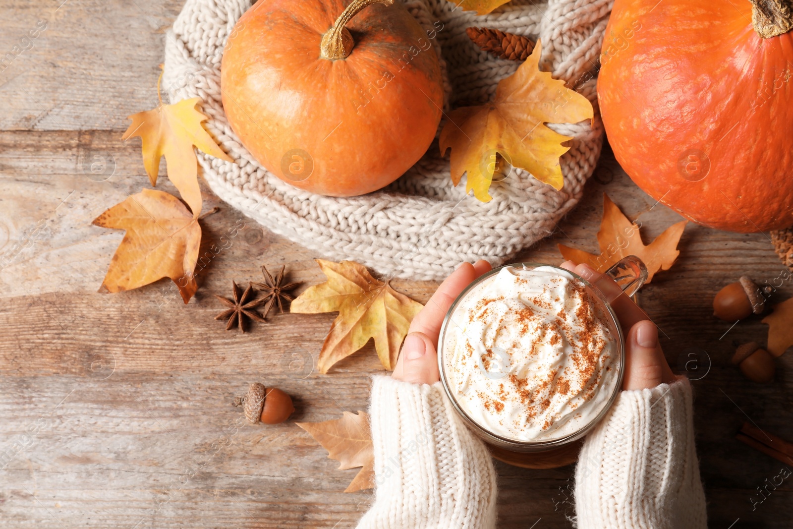 Photo of Woman holding cup with pumpkin spice latte on wooden table, flat lay