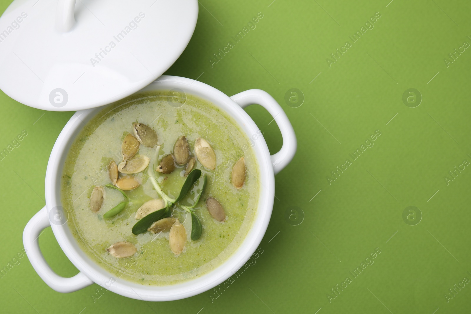 Photo of Delicious broccoli cream soup with pumpkin seeds on green background, top view. Space for text