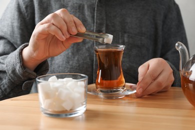 Woman adding sugar cube into aromatic tea at wooden table, closeup