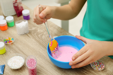 Photo of Little girl mixing ingredients with silicone spatula at table, closeup. DIY slime toy