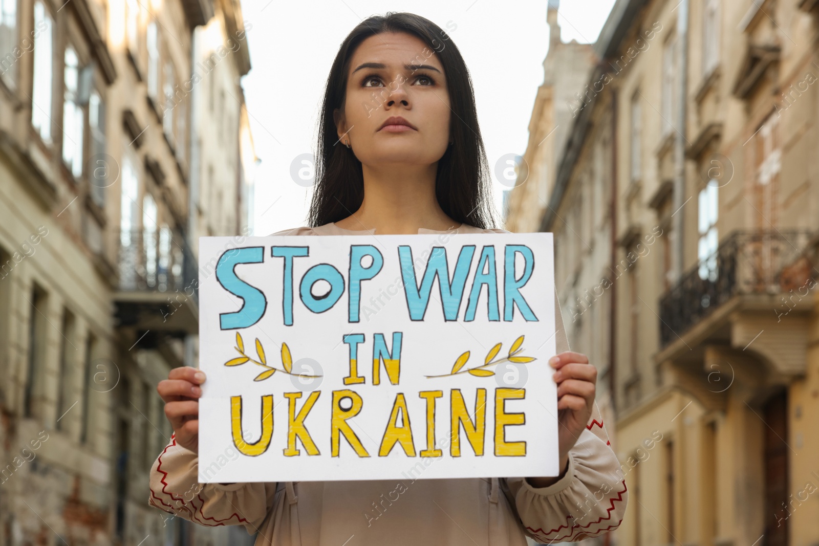 Photo of Sad woman holding poster Stop War in Ukraine on city street