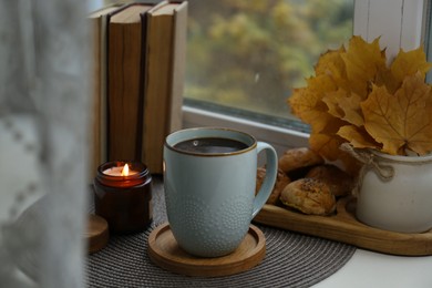 Photo of Cup of tasty hot drink near books, burning candle and cookies on windowsill. Autumn coziness
