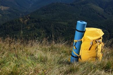 Backpack and sleeping pad in mountains on sunny day, space for text