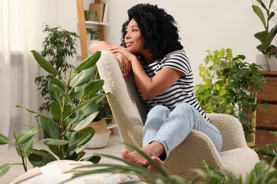 Woman relaxing in armchair surrounded by beautiful houseplants at home