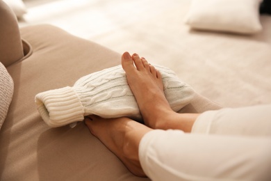 Woman warming feet with hot water bottle on sofa, closeup