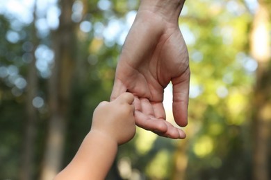 Daughter holding father's hand outdoors, closeup. Happy family