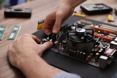 Photo of Male technician repairing motherboard at table, closeup