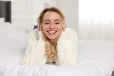 Photo of Happy woman in stylish warm sweater lying on bed indoors