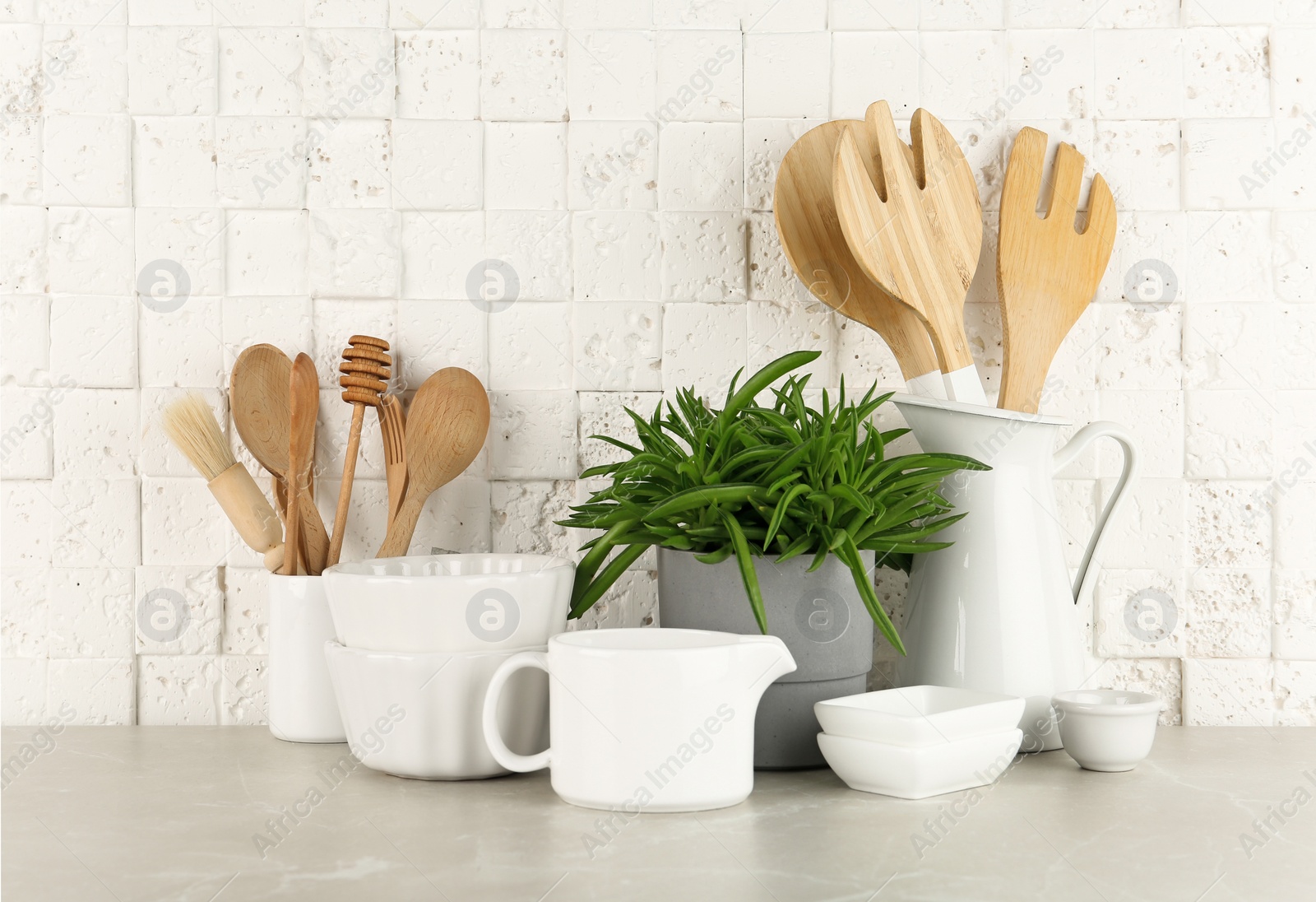 Photo of Green plant and different kitchenware on table near brick wall. Modern interior design