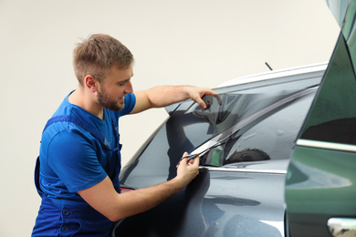 Worker tinting car window with foil in workshop