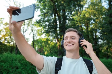 Smiling man in headphones taking selfie in park