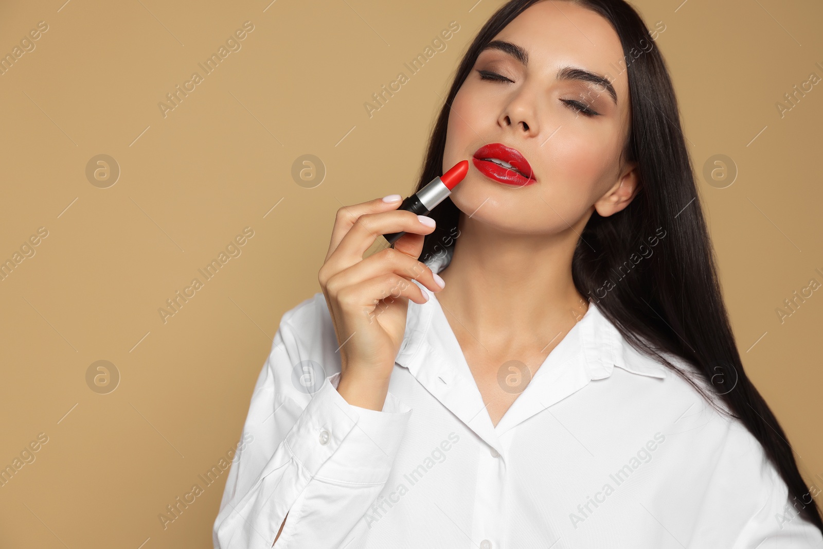Photo of Young woman with beautiful makeup holding red lipstick on beige background