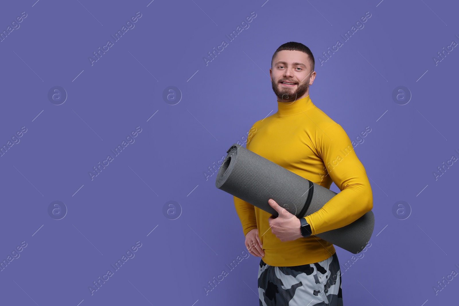 Photo of Handsome man with fitness mat on purple background, space for text