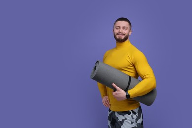 Photo of Handsome man with fitness mat on purple background, space for text