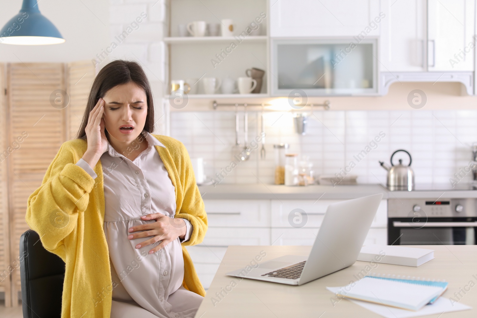 Photo of Young pregnant woman suffering from headache in home office