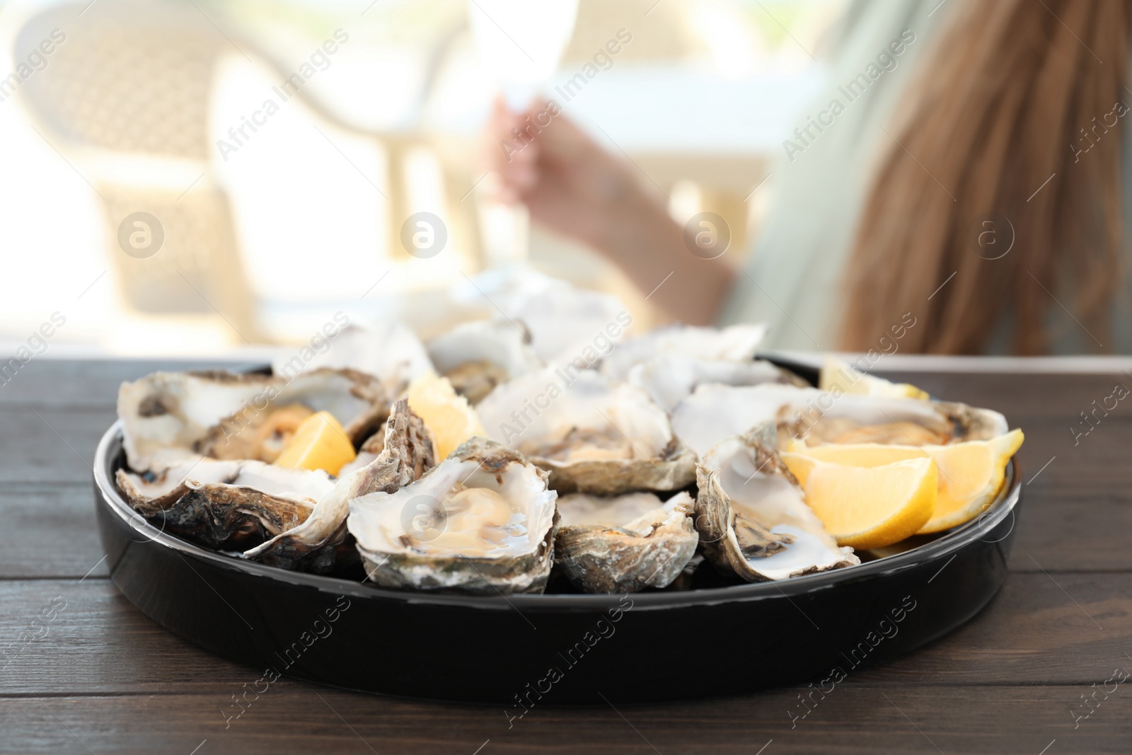 Photo of Fresh oysters with cut juicy lemon and woman at table