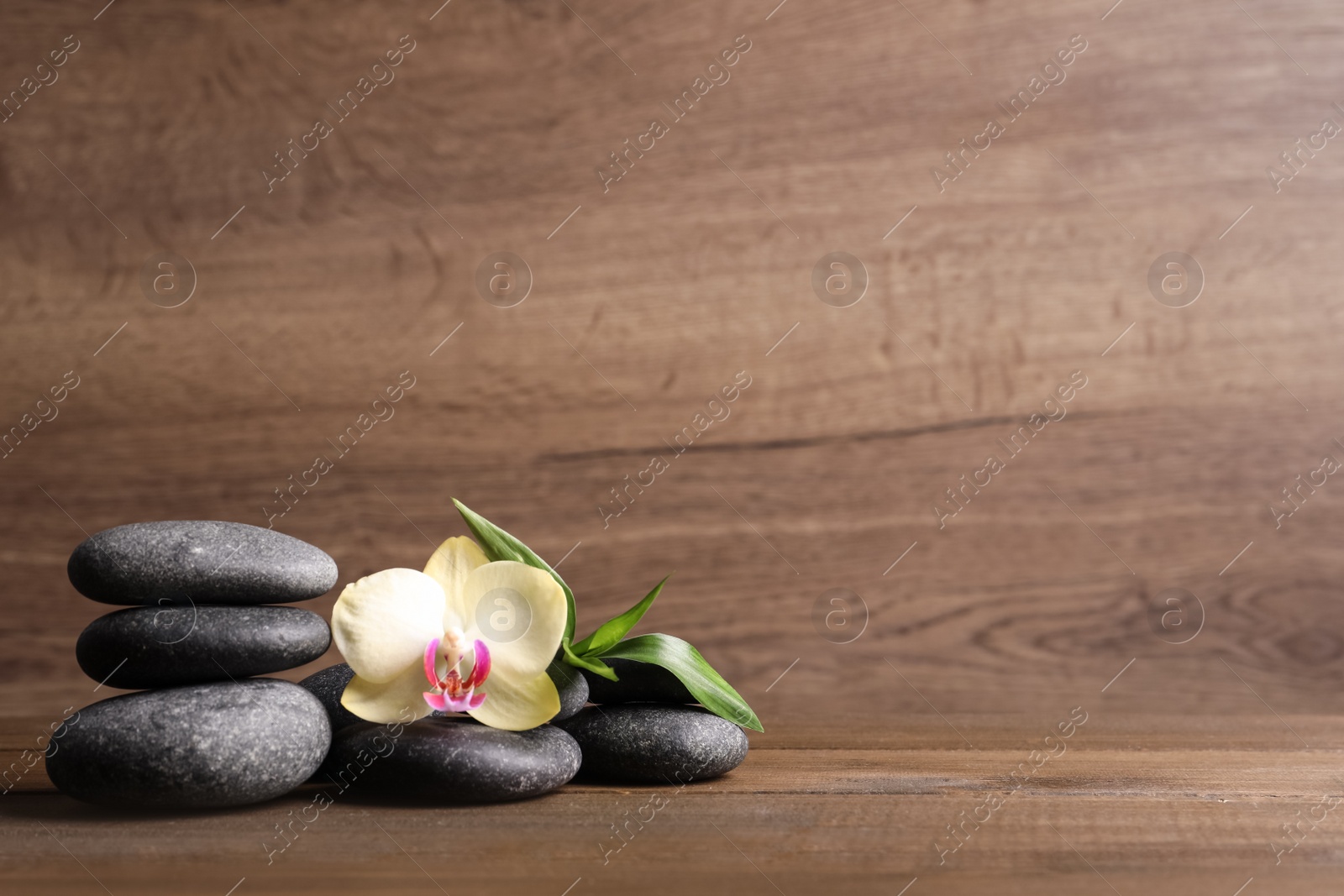 Photo of Spa stones, beautiful orchid flower and bamboo sprout on wooden table. Space for text