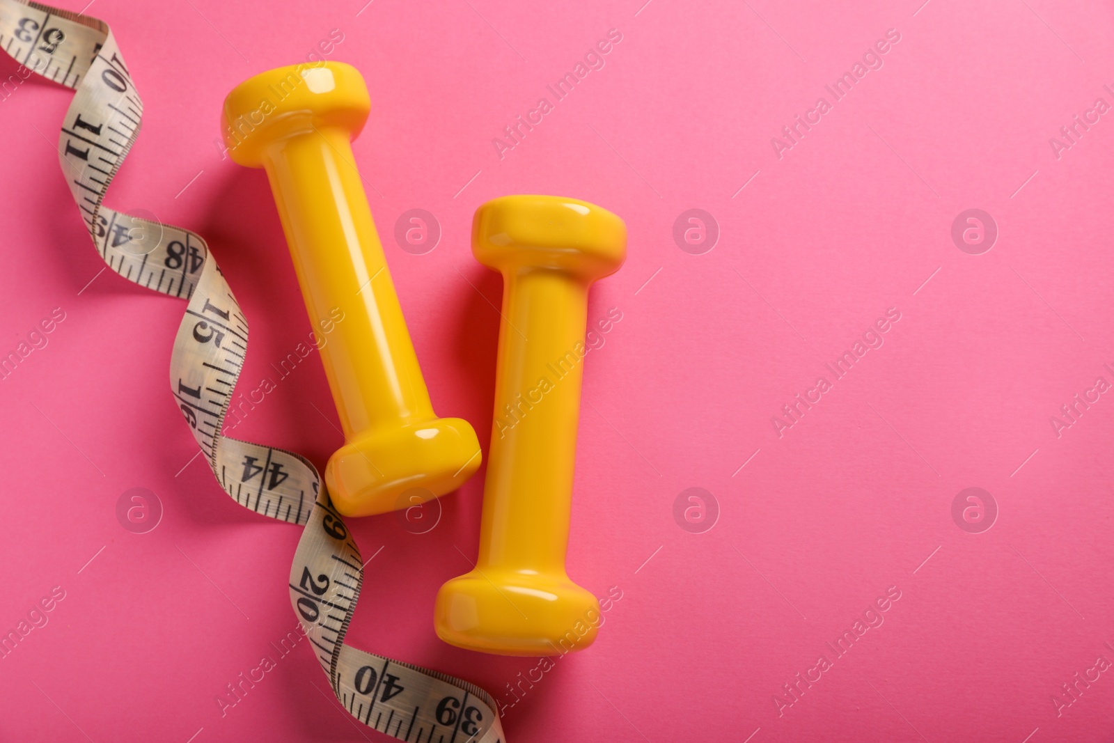 Photo of Measuring tape and dumbbells on pink background, flat lay with space for text. Weight control concept